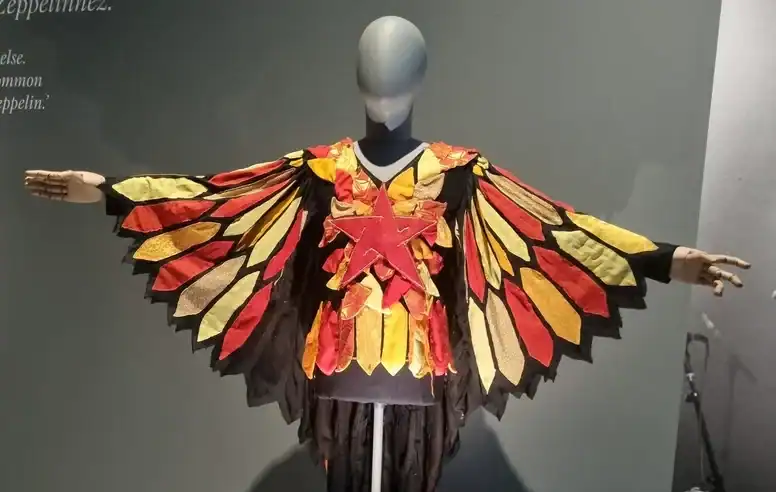 Life-sized mannequin wearing a multicolored feathered winged costume with a red star chest piece, arms extended in a museum display.