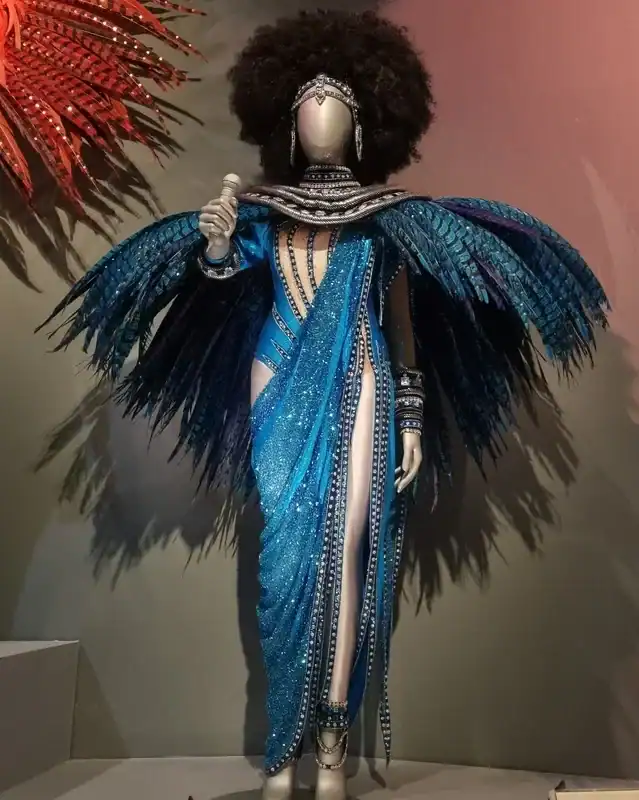 Mannequin wearing a turquoise-blue carnival costume with large feathered wings and beaded bodice.