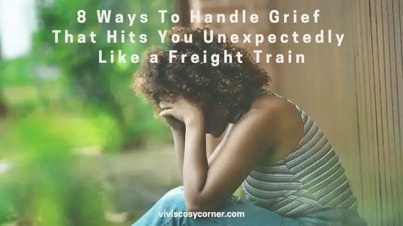Sad woman with curly hair sitting against a wooden fence, head resting on her hands, conveying grief and distress (blog header: '8 Ways To Handle Grief That Hits You Unexpectedly Like a Freight Train').