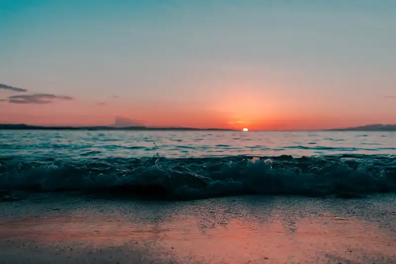 Sunset over the ocean with gentle waves reaching a sandy beach, pink and orange sky reflecting on the water." ,